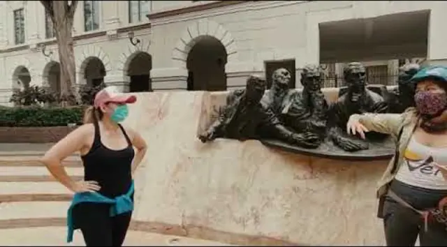 Video still: a walking group beside a bronze monument in Guayaquil